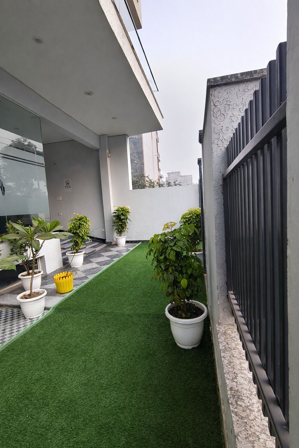 A rooftop terrace with artificial grass, potted plants, and a modern building facade.