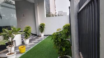 A rooftop terrace with artificial grass, potted plants, and a modern building facade.