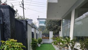 A narrow courtyard with artificial green turf, potted plants, and a modern building facade. - Hotel Stayzzy Bloom (Noida)