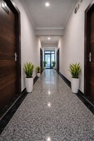 A hallway with dark wooden doors, white walls, and a polished granite floor. There are potted plants on either side of the hallway.