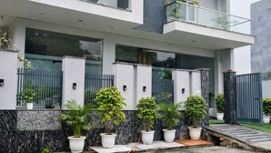 A modern two-story house with a balcony, large windows, and a variety of potted plants along the front wall. - Hotel Stayzzy Bloom (Noida)