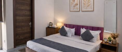 A bedroom with a bed, bedside tables, a nightstand, a wall-mounted air conditioner, and two framed leaf artworks.