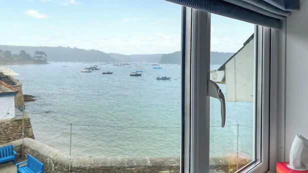 A view from a window overlooking a calm body of water with several boats, a stone wall, and a blue bench. - 3 bedroom accommodation in St Mawes (St Mawes)