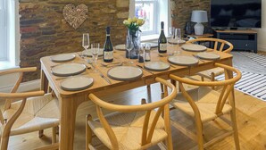 A dining area with a stone wall, wooden table, and chairs. - 3 bedroom accommodation in St Mawes (St Mawes)