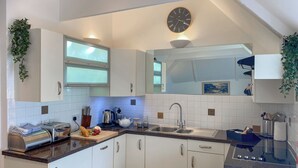 A modern kitchen with white cabinets, a built-in oven, a sink, and a clock on the wall. - 3 bedroom accommodation in St Mawes (St Mawes)