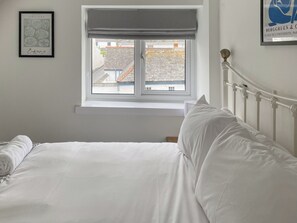 Un lit bien fait dans une chambre avec une fenêtre, une œuvre d’art encadrée au mur et une tête de lit en métal.