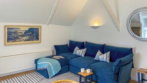 A cozy room with a blue sectional sofa, a small table with two cups, a framed picture on the wall, and a mirror. - 3 bedroom accommodation in St Mawes (St Mawes)