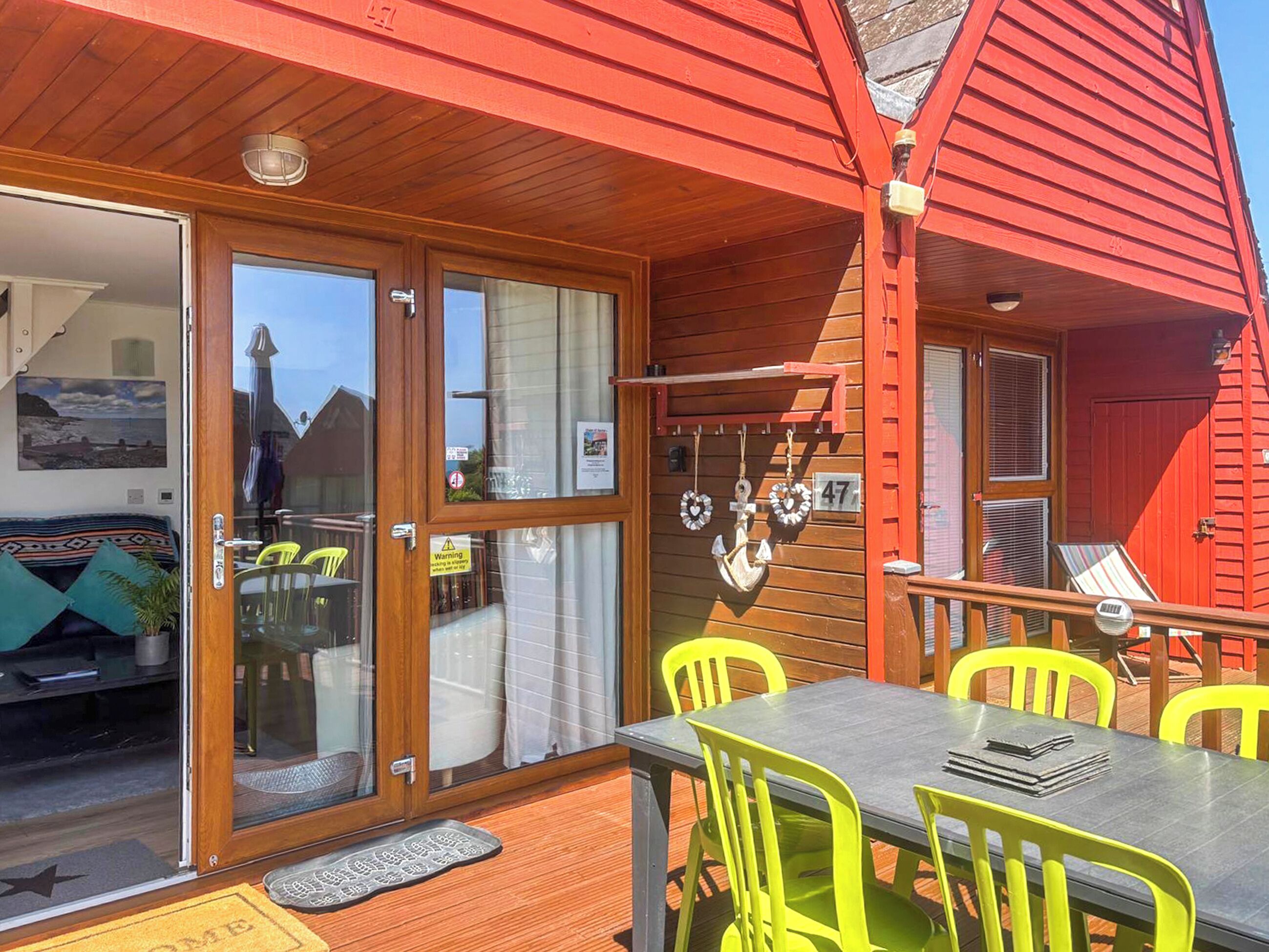 En træterrasse med et bord og stole, en skydedør i glas samt en rød facade.