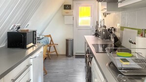 Eine moderne Küche mit Mikrowelle, Toaster und Wasserkocher. Ein Stuhl und ein Mülleimer sind vorhanden.