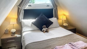 Ein Hotelzimmer mit einem Bett, zwei Nachttischen, einem Fenster mit Vorhängen und Blick auf den Himmel.