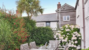 A wooden outdoor table with chairs, surrounded by lush greenery and flowering plants. - 3 bedroom accommodation in Bude (Bude)