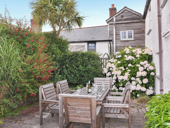 A wooden outdoor table with chairs, surrounded by lush greenery and flowering plants.