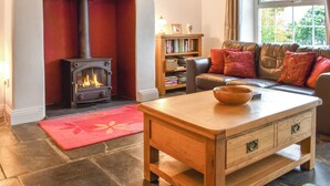 A cozy living room with a fireplace, a leather sofa, a wooden coffee table, and a bookshelf. - 3 bedroom accommodation in Bude (Bude)