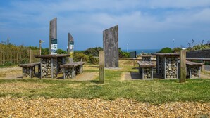 A coastal area with wooden structures, possibly a park or a historical site, with informational signs and benches.