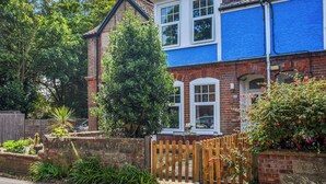 A two-story house with a blue exterior, a brick chimney, and a wooden fence.