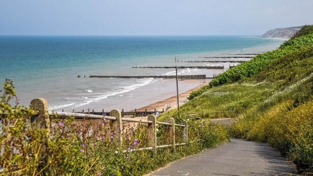 A coastal road leading to a beach with a wooden fence and a stone wall.