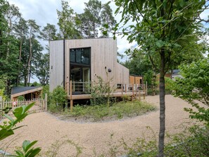 A modern wooden cabin with a deck, surrounded by trees and gravel. - Unique design holiday home in a quiet location (Biron)