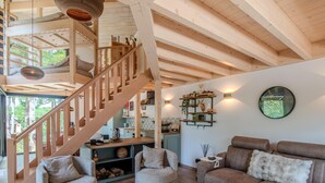Een ruime woonkamer met een houten trap, comfortabele zithoek en een keuken op de achtergrond.