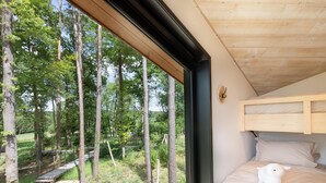 Een slaapkamer met een groot raam, een stapelbed en uitzicht op een bebost gebied.