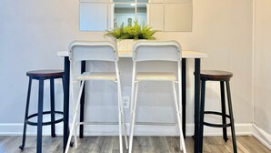 Un coin repas avec une table blanche, deux chaises blanches et deux tabourets noirs.
