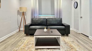 Un salon moderne avec un canapé en cuir noir, une table basse en bois, un lampadaire et une fenêtre avec des rideaux.