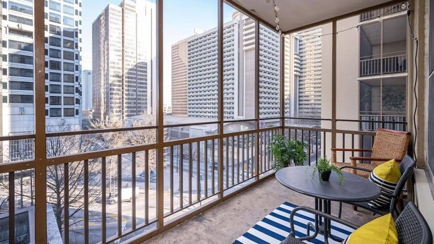 Ein Balkon mit Blick auf hohe Gebäude, einem runden Tisch mit Stühlen und einem Blumentopf.