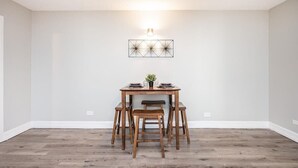 Ein Essbereich mit Holztisch, vier Stühlen, einer Wandleuchte und einem geometrischen Wandbild.
