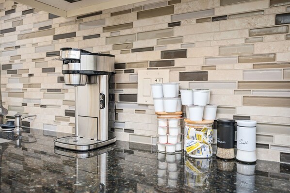 A coffee machine, disposable cups, and salt and pepper shakers on a kitchen counter.