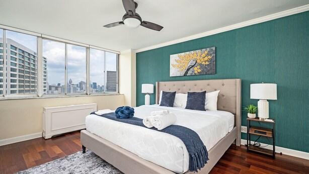 Un dormitorio con una cama grande, ventilador de techo, vista a la ciudad y una pared de acento verde.