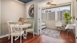 Un comedor con una mesa y sillas blancas, un ventilador de techo y vistas a edificios a través de un ventanal.