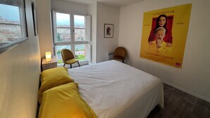 A hotel room with a bed, two chairs, a window, and a poster on the wall. - Bright apartment overlooking the Tarn (Albi)