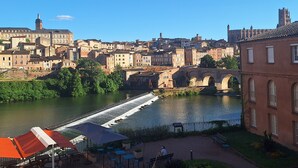 A riverside view of a historic town with a bridge, buildings, and a riverside café with outdoor seating. - Bright apartment overlooking the Tarn (Albi)