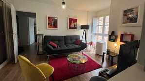 A modern living room with a black sofa, a yellow chair, a red rug, and artwork on the walls. - Bright apartment overlooking the Tarn (Albi)