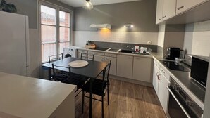 A modern kitchen with a dining area, built-in appliances, and a large window providing natural light. - Bright apartment overlooking the Tarn (Albi)