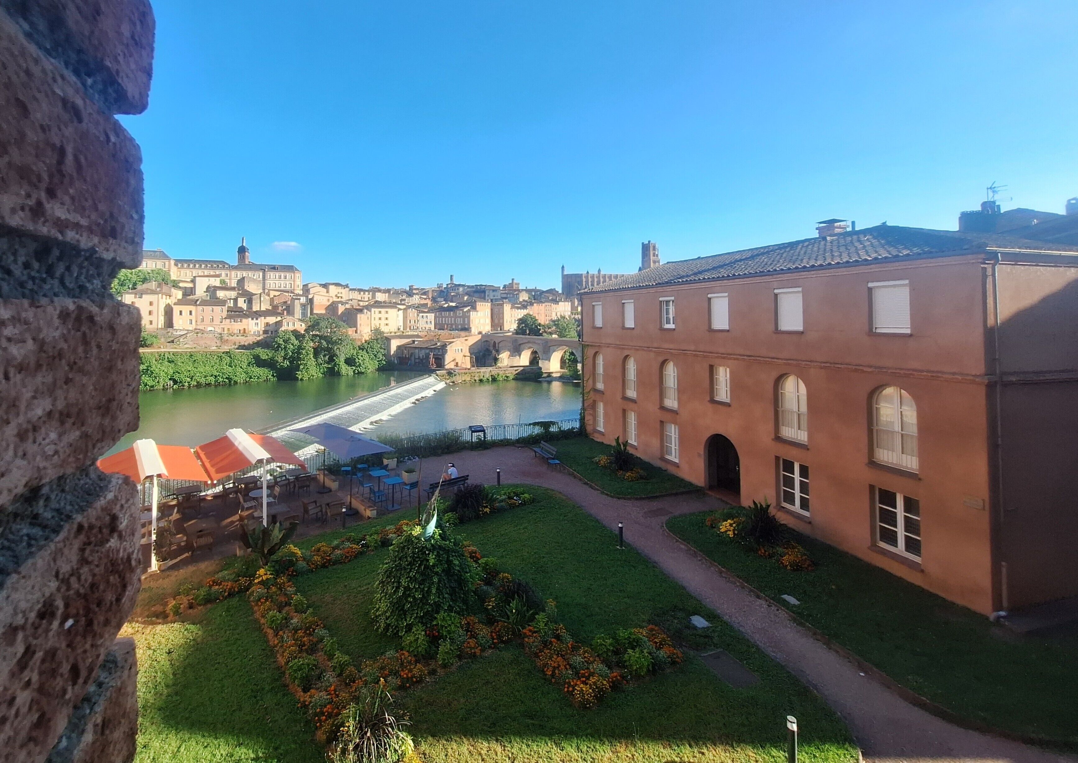 A courtyard with a river, a brick building, and a view of a historic town.