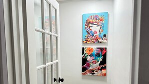 A hallway with a white door and two vibrant paintings on the wall.