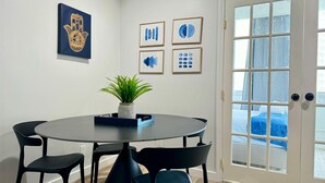 A dining area with a round table, four black chairs, a potted plant, and artwork on the wall.