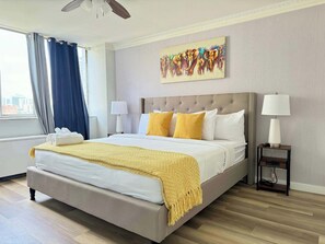 Un cuarto de hotel con una cama grande, dos lámparas de noche, un cuadro en la pared y vistas de la ciudad a través de la ventana.