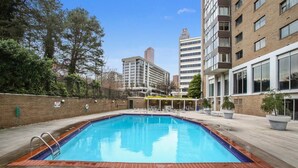 A rectangular swimming pool with a tiled edge, surrounded by a brick wall and a paved deck.