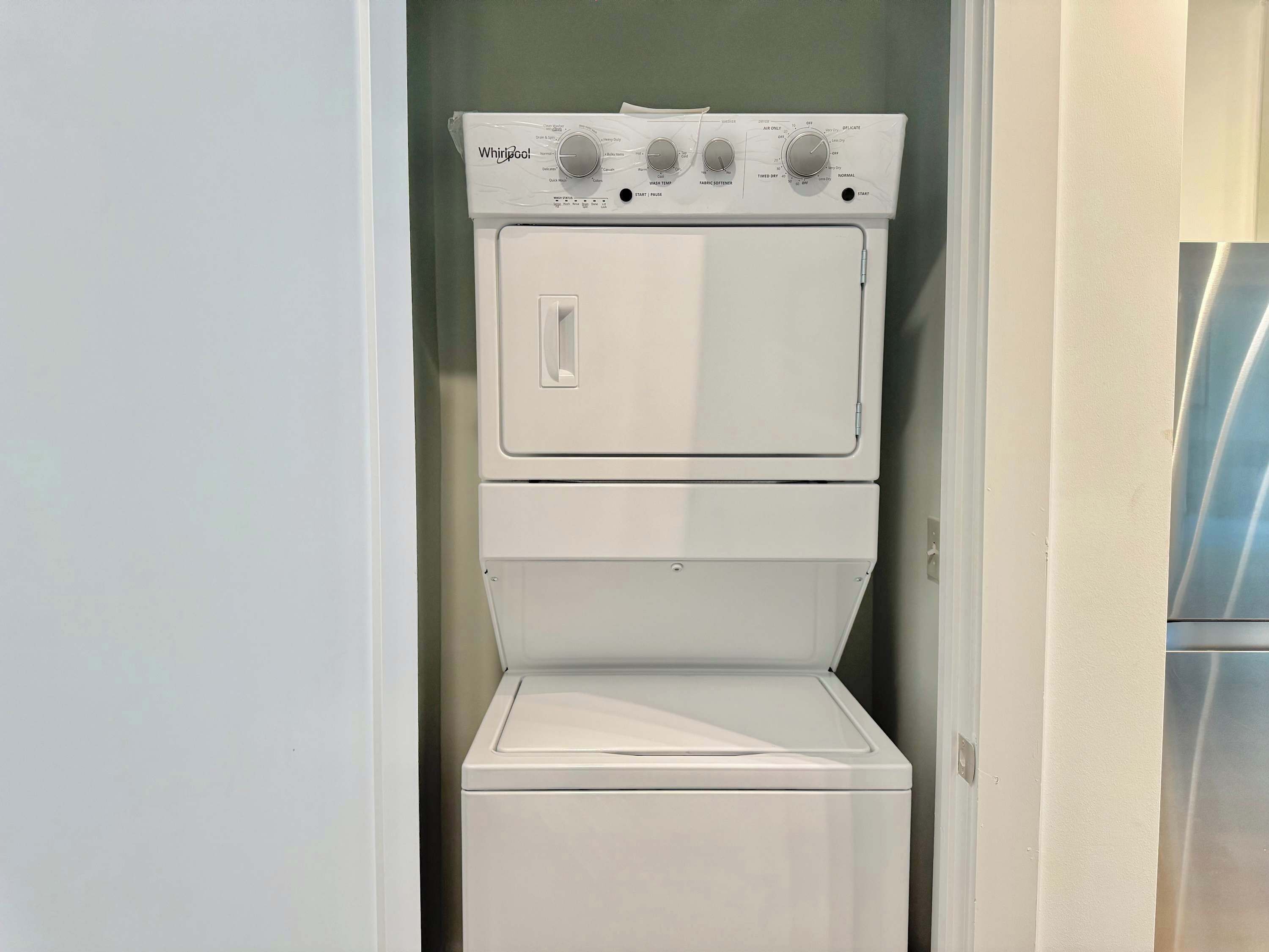 A stacked washer and dryer unit in a small laundry room with a door leading to a hallway.