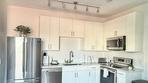 A modern kitchen with white cabinets, stainless steel appliances, and a microwave. - Upgraded Apartment in Old Fourth Ward w/ Patio (Atlanta)