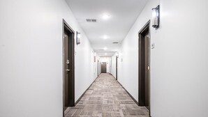 A long, narrow hallway with carpeted floors and white walls, featuring doors on both sides and a central light fixture. - Upgraded Apartment in Old Fourth Ward w/ Patio (Atlanta)