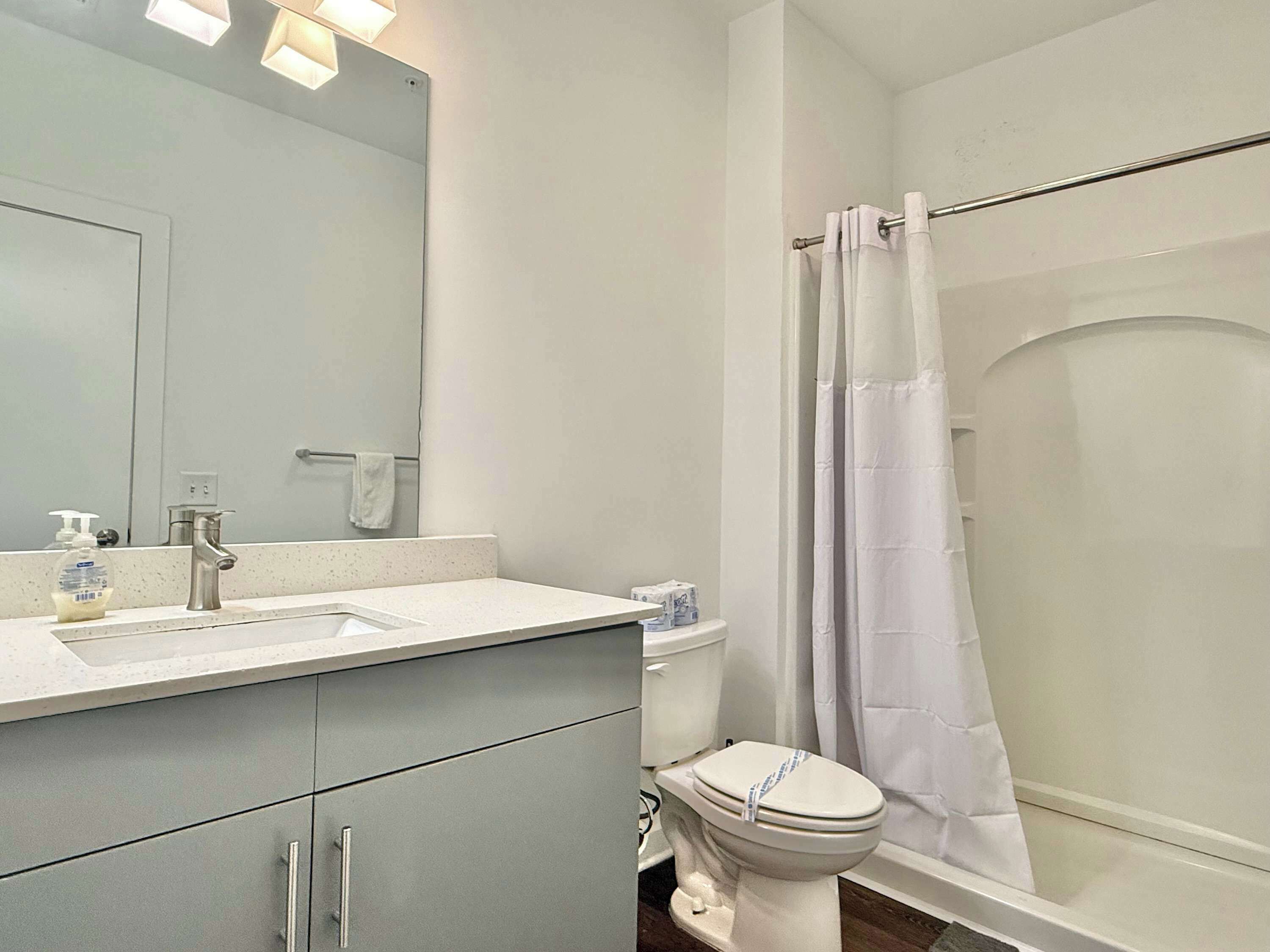 Et badeværelse med vask, spejl, toilet og bruseforhæng.