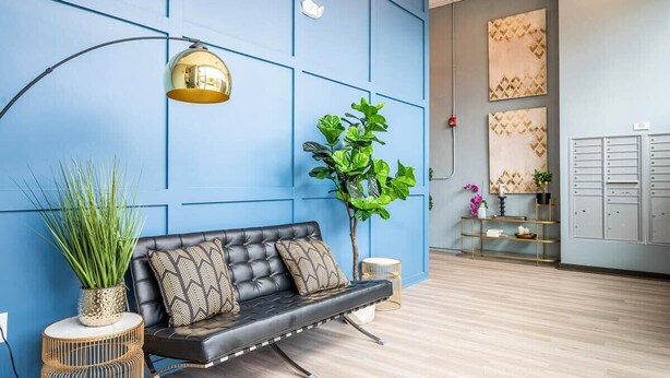 A modern lobby with a black leather sofa, a large green plant, and a gold pendant light. - Upgraded Apartment in Old Fourth Ward w/ Patio (Atlanta)