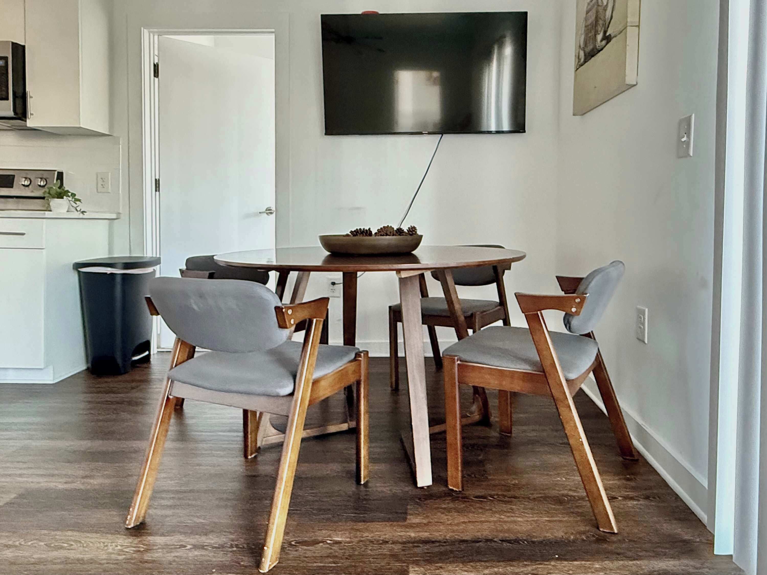 Ein Essbereich mit einem runden Tisch, vier Holzstühlen und einem an der Wand befestigten Flachbildfernseher.