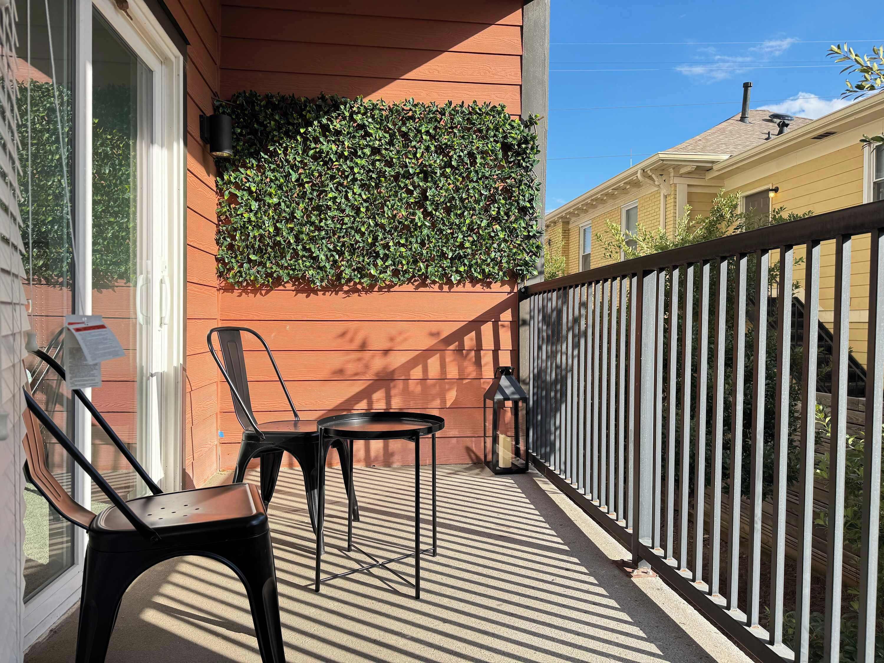 A balcony with a black metal chair and a small table, a potted plant, and a metal fence.