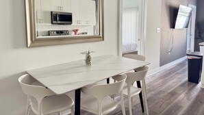 A modern kitchen with white cabinets, a microwave, and a dining area with a marble table and white chairs.