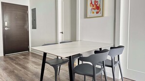 A modern dining area with a white table and four chairs, a dark wooden door, and a framed abstract painting on the wall.
