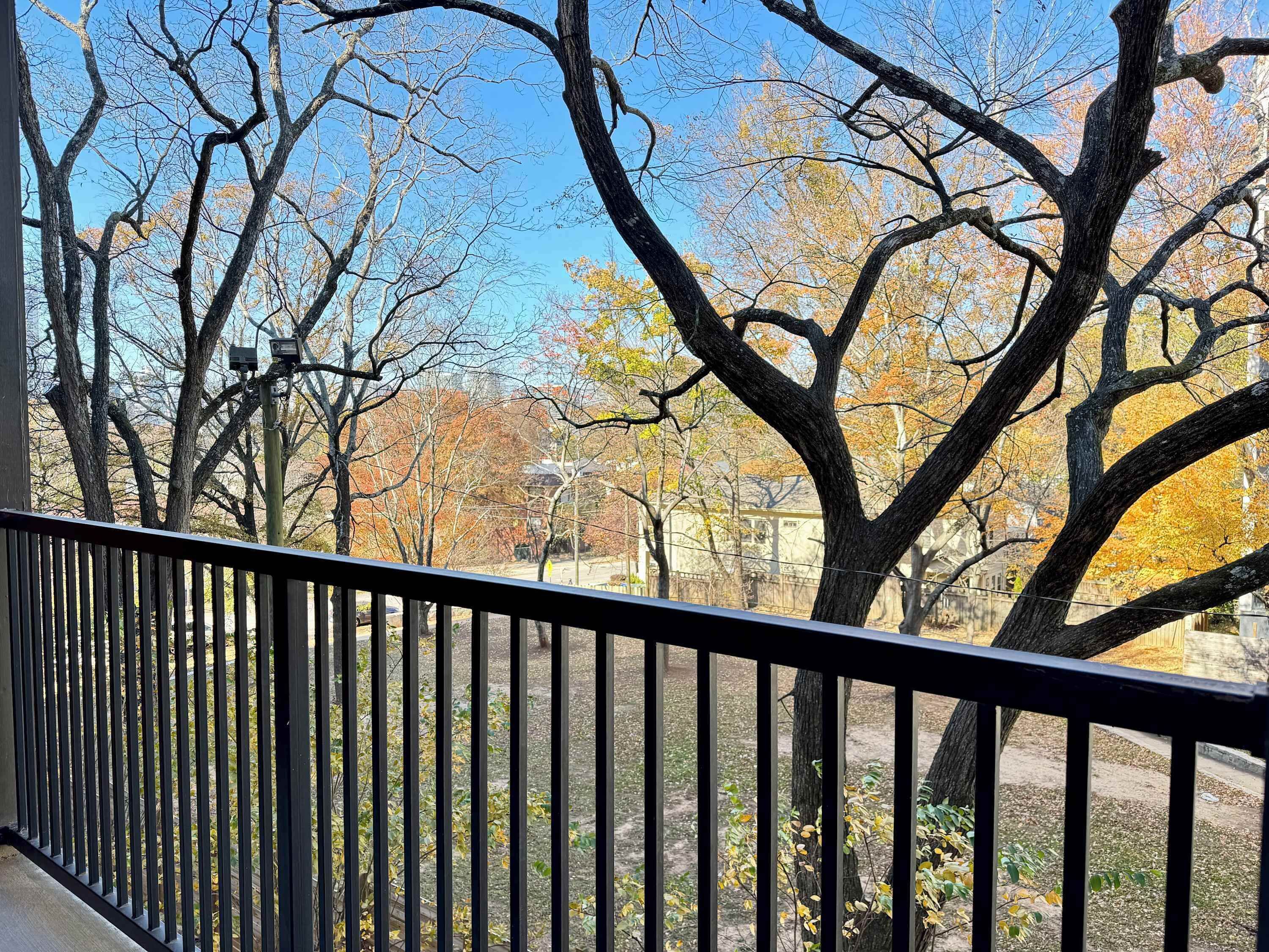 Un balcon donnant sur des arbres, avec un bâtiment visible au loin.