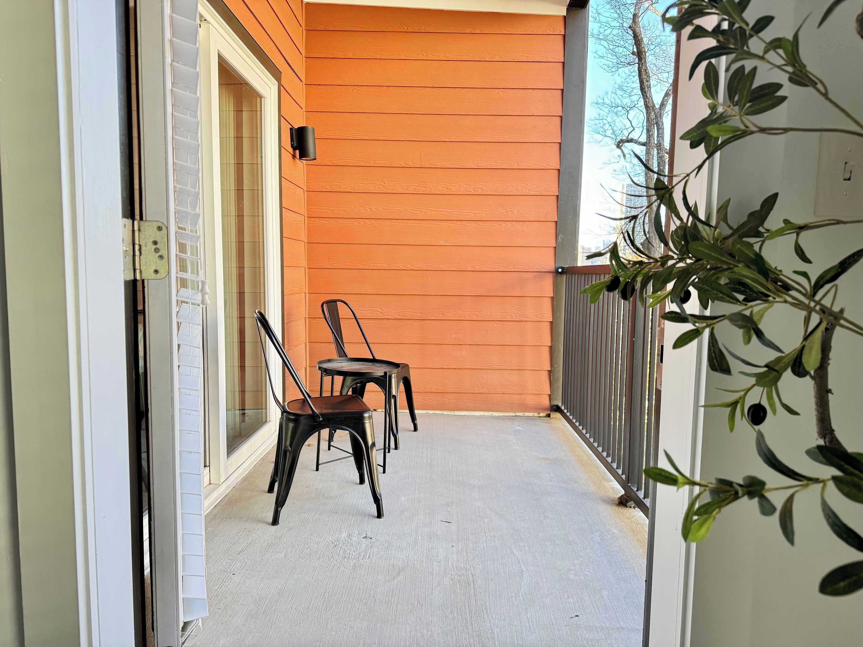 A balcony with two chairs and a small table, wooden walls, and a metal railing.